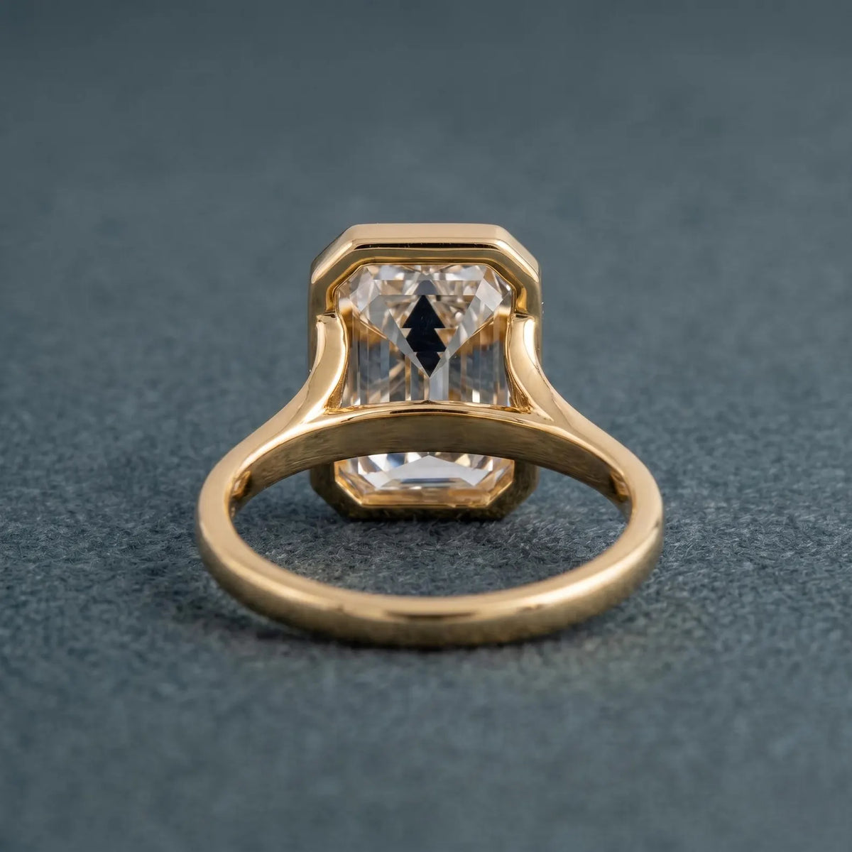 Underside view of a 3 carat emerald cut lab diamond ring displaying the open-back bezel setting and polished gold shank.