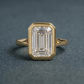 Direct top-down view highlighting the step-cut facets and protective yellow gold bezel frame of a 3 carat emerald lab diamond.