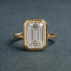 Direct top-down view highlighting the step-cut facets and protective yellow gold bezel frame of a 3 carat emerald lab diamond.