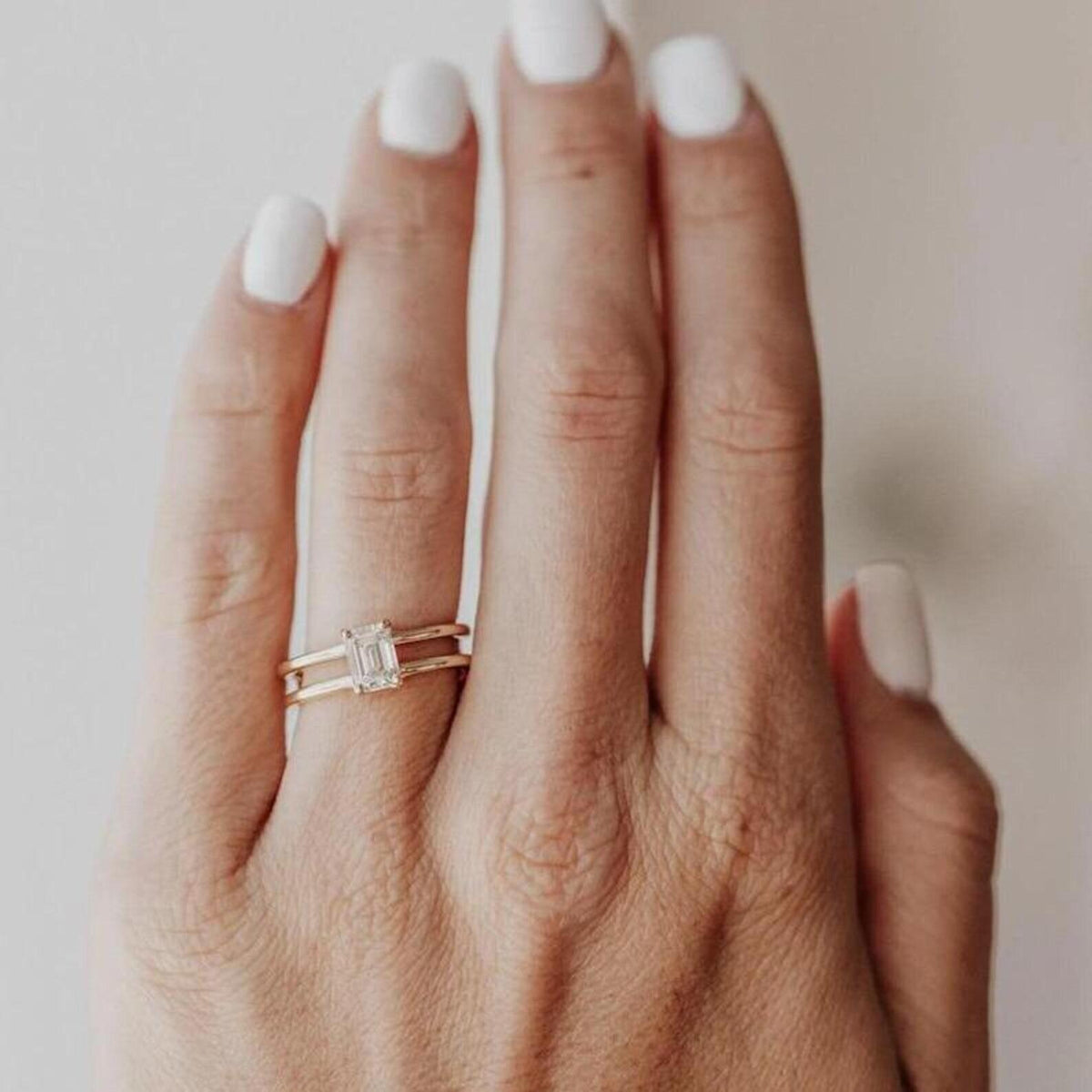On-hand view of a 2 CT emerald cut lab grown diamond engagement ring with double gold band.