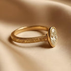 Side angle view of a 2 CT oval lab grown diamond bezel engagement ring in yellow gold with hand-engraved band.