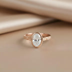 Rose gold 2 carat oval lab grown diamond bezel solitaire engagement ring on soft neutral background.