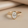 Front view of 2 CT oval lab grown diamond engagement ring with bezel setting and milgrain detailing in yellow gold.