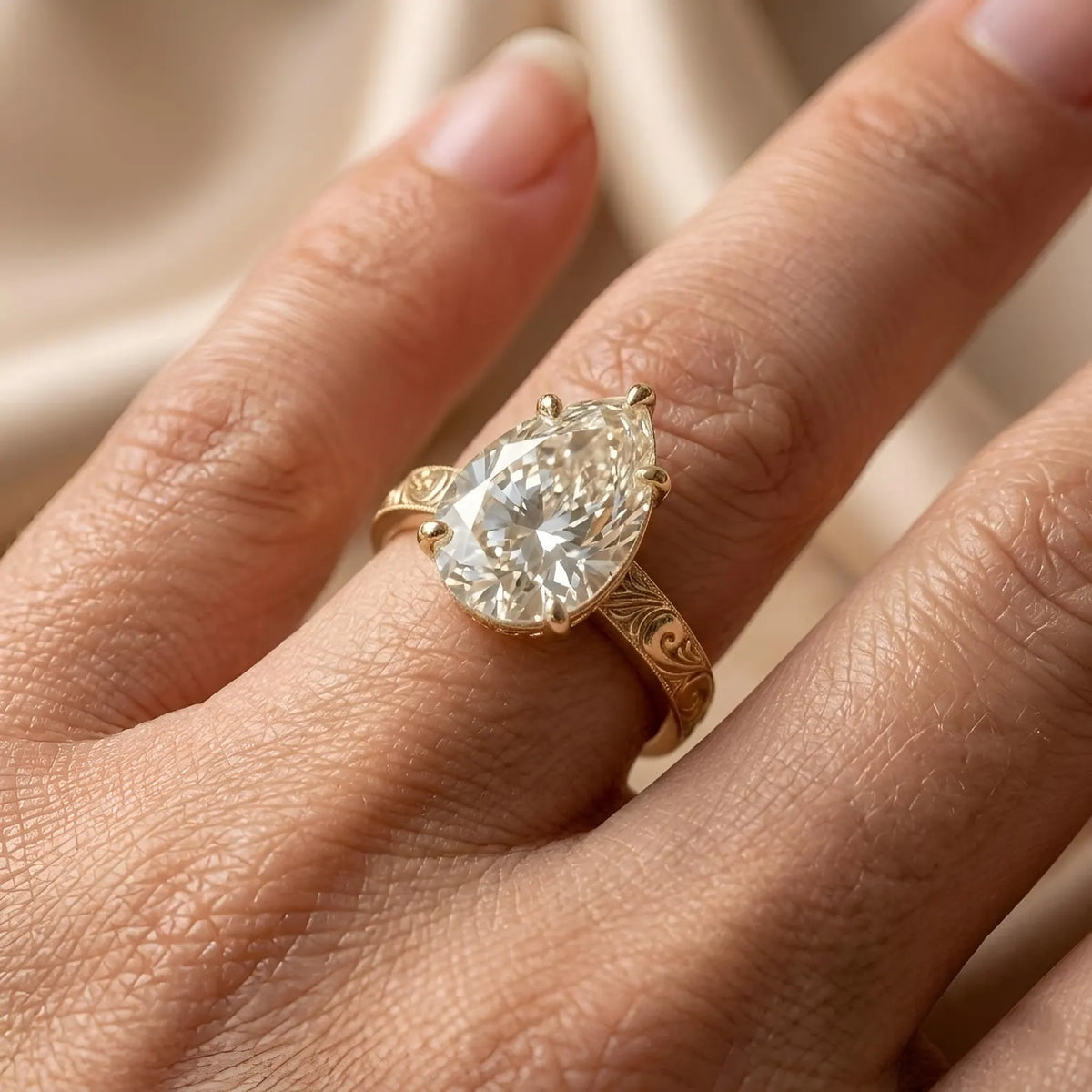 On-hand view of a 3 CT pear lab grown diamond engagement ring with hand-engraved gold band.