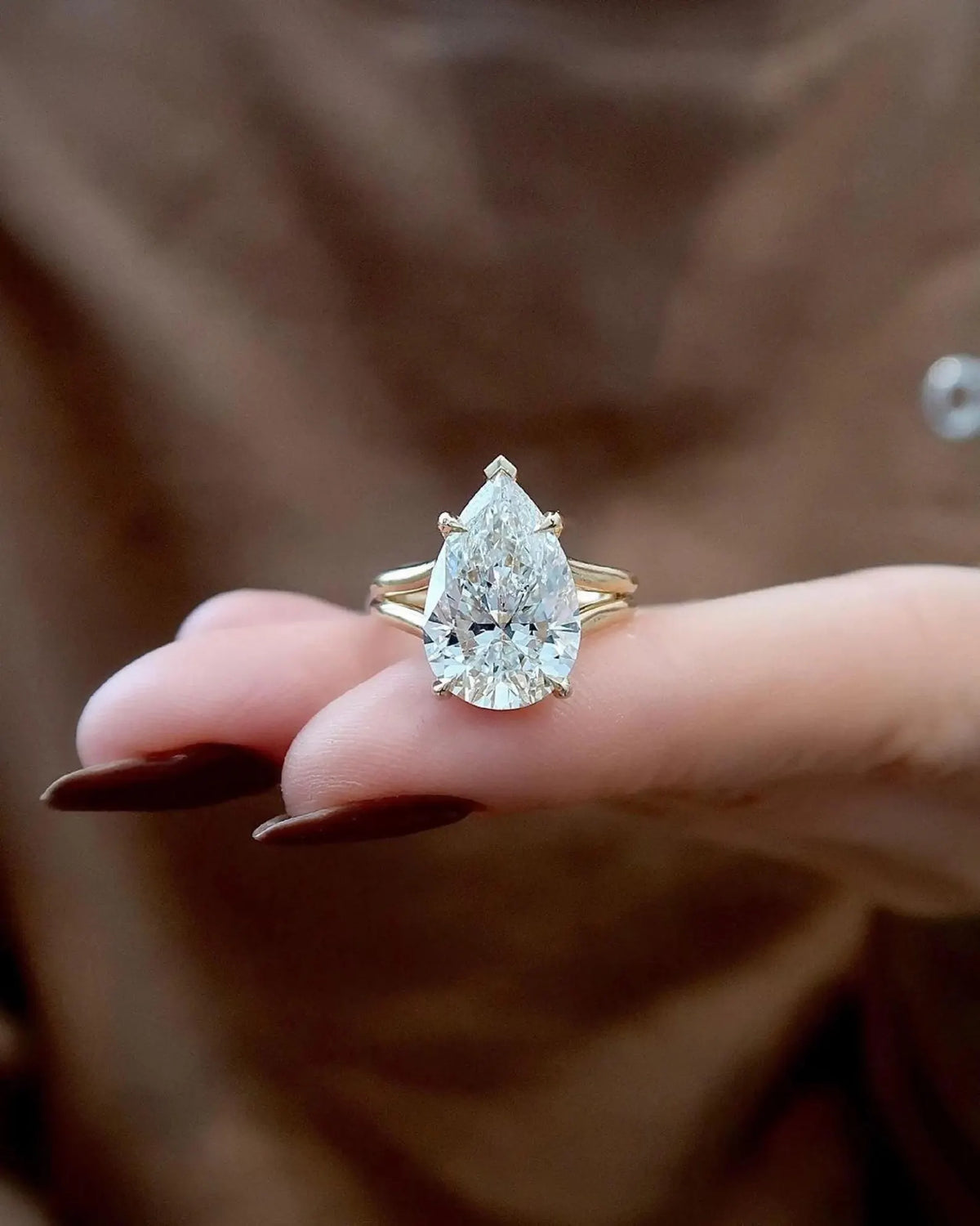 Close-up view of a 4 carat pear lab created diamond sitting on fingers showing claw prongs and split band.