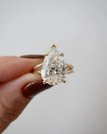 Front close-up view of a 4 CT pear cut lab diamond engagement ring held in hand with yellow gold double band.