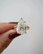 Front close-up view of a 4 CT pear cut lab diamond engagement ring held in hand with yellow gold double band.