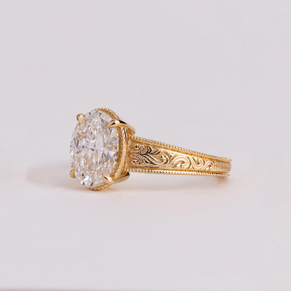 Side profile shot showcasing 4-prong setting, milgrain rim, and detailed floral scrollwork engraving on yellow gold band.