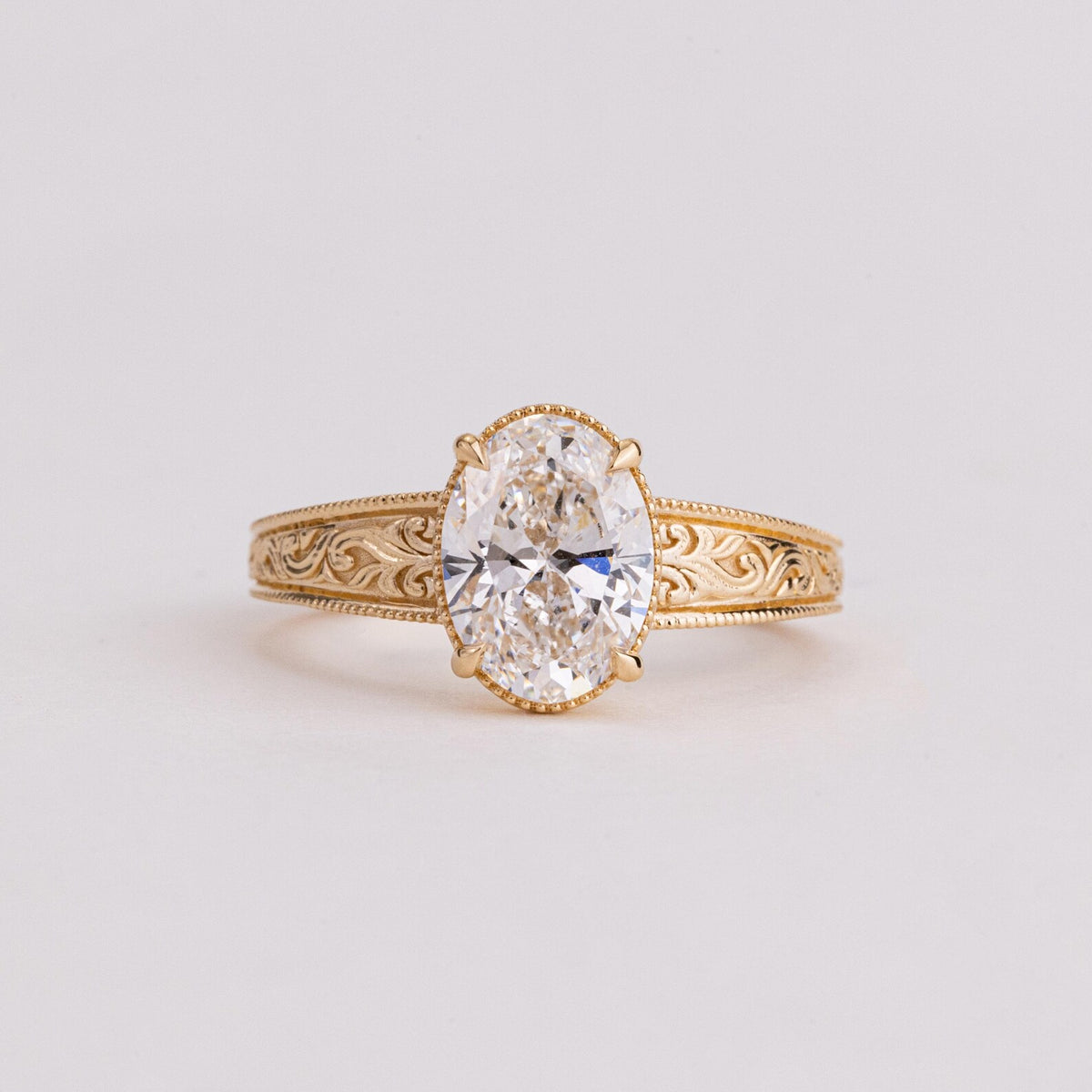 Frontal close-up view of a 2 CT oval lab created diamond solitaire ring with milgrain trim and engraved band.