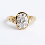 Top-down view showing the brilliance of a 3ct oval lab-created diamond in a bezel setting with star accents on yellow gold.