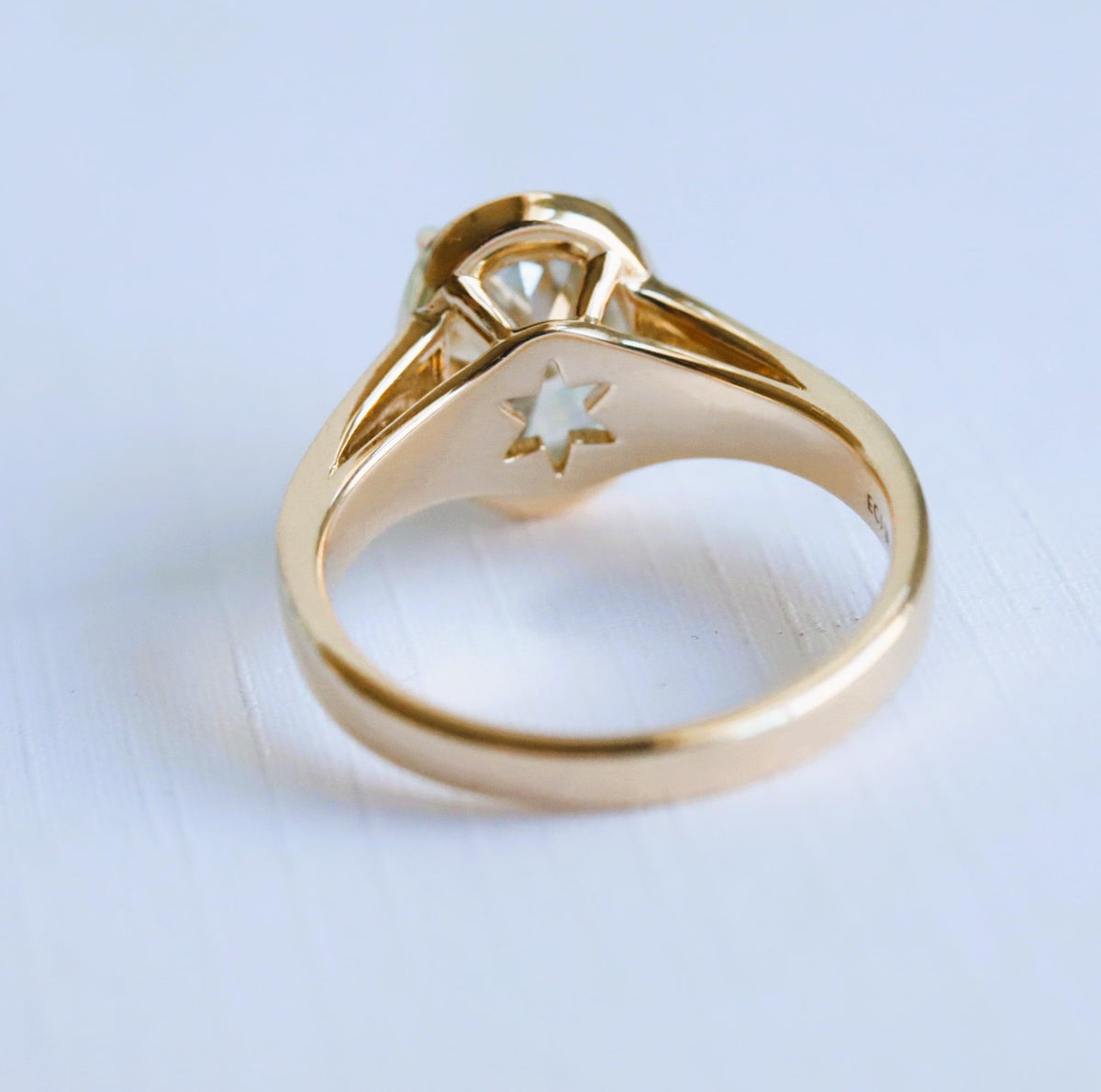 Underside view of a 3 carat oval lab grown diamond engagement ring in gold showing a star-shaped basket cut-out and thick gold band.