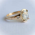 Side profile of a 3 ct oval lab diamond ring featuring starburst engravings set with small diamond accents on a gold band.