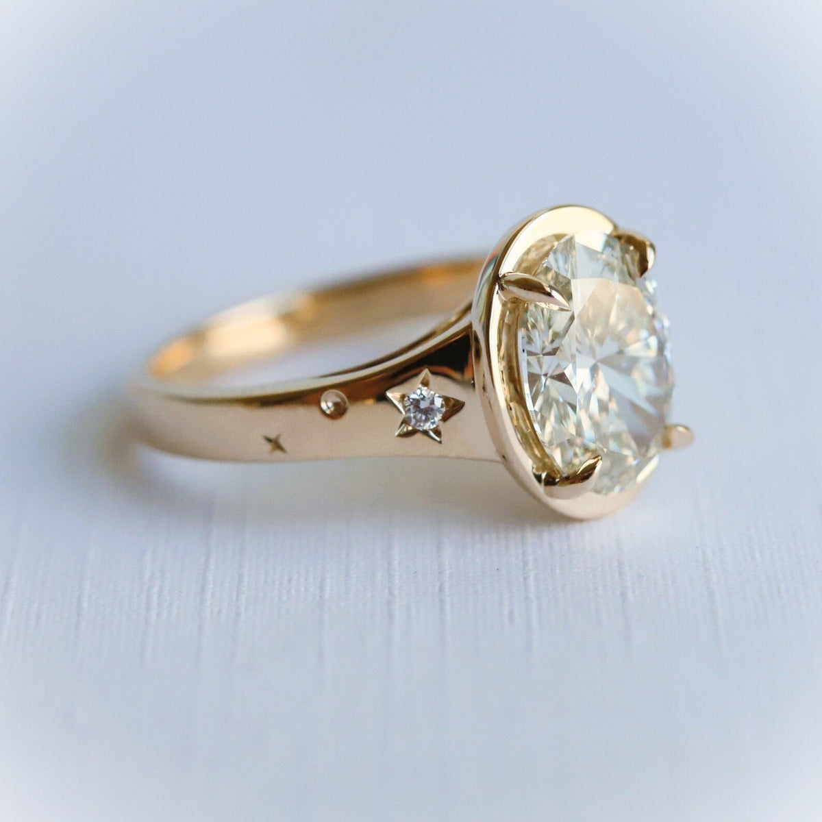 Side profile of a 3 ct oval lab diamond ring featuring starburst engravings set with small diamond accents on a gold band.