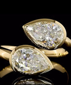 Macro close-up of two bezel-set pear cut lab grown diamonds on an open yellow gold Toi et Moi ring.