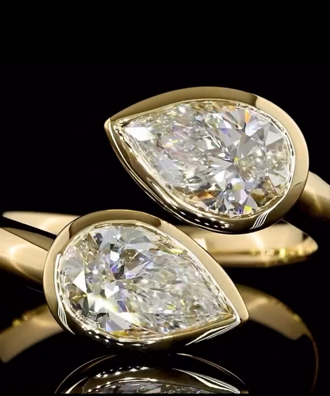 Macro close-up of two bezel-set pear cut lab grown diamonds on an open yellow gold Toi et Moi ring.