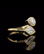 Side perspective view highlighting the smooth yellow gold band and bezel-encased dual pear lab diamonds.
