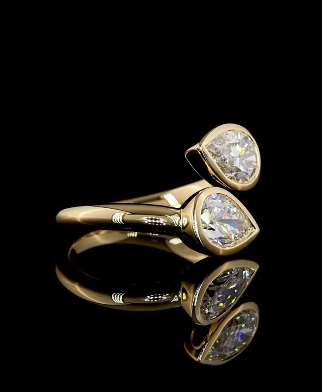 Side perspective view highlighting the smooth yellow gold band and bezel-encased dual pear lab diamonds.