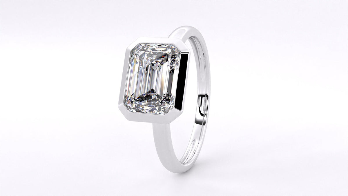 Under-gallery and profile view of a sleek white gold ring featuring a bezel-set emerald cut diamond.