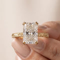 Hand holding a 5 CT radiant cut lab diamond solitaire ring detailing the yellow gold milgrain edge and scroll work.