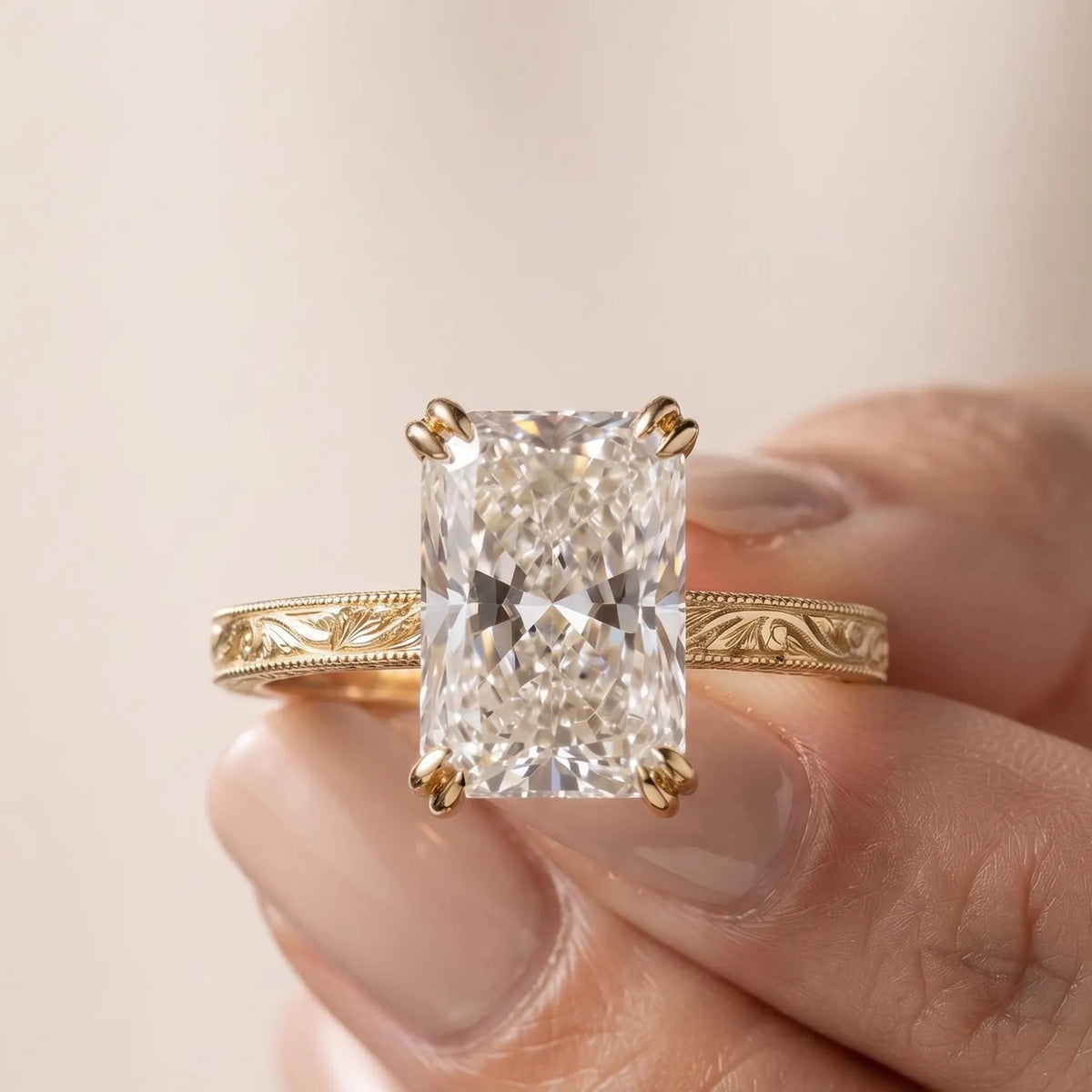 Hand holding a 5 CT radiant cut lab diamond solitaire ring detailing the yellow gold milgrain edge and scroll work.