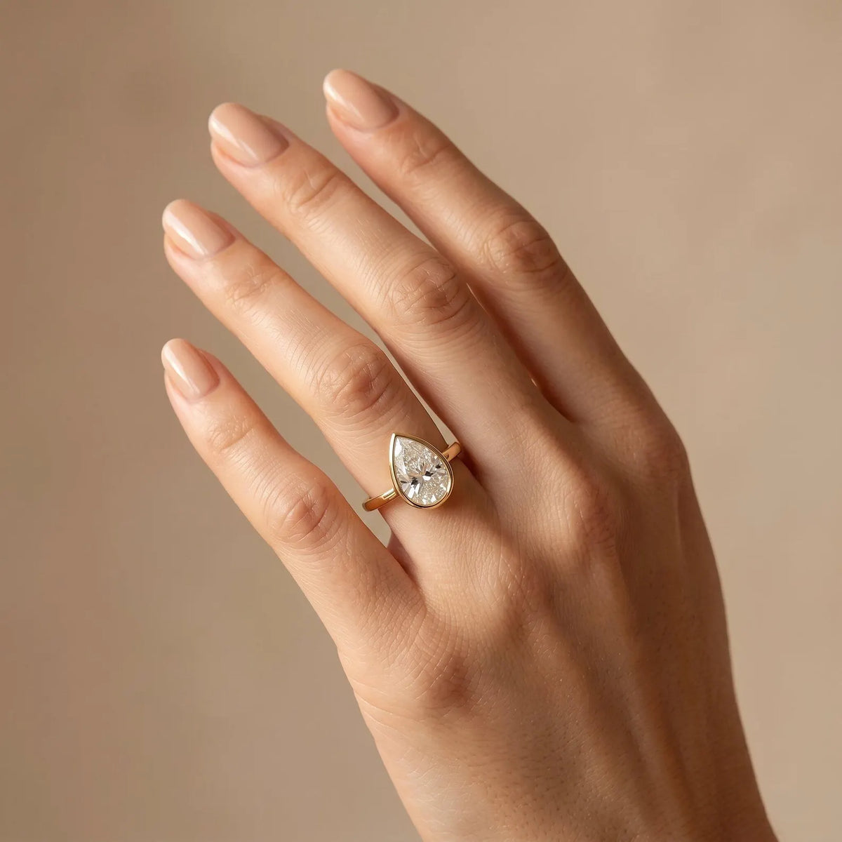 3 CT pear cut lab-grown diamond engagement ring in a sleek yellow gold bezel setting worn on a finger.