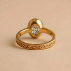 Underside view of a 2 carat oval diamond ring showing the solid gold bezel setting and floral carved shank.