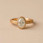 Front view of a 2 CT oval lab diamond framed in a milgrain yellow gold bezel setting.