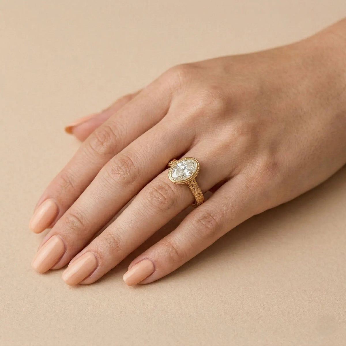 2 CT oval lab-grown diamond engagement ring with engraved yellow gold band worn on hand.