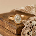 Antique style 2 carat oval lab diamond engagement ring resting on a wooden box with crocheted lace background.