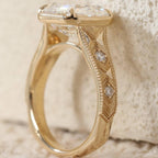 Profile view of a vintage-inspired 3 CT Asscher lab diamond engagement ring showing gold milgrain border and detailed filigree shank.