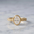 3 CT oval lab-grown diamond engagement ring in yellow gold milgrain bezel with hand-engraved scrollwork sitting on marble.