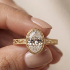 Hand holding a 3 carat oval lab diamond ring displaying intricate vintage scrollwork on the gold band.