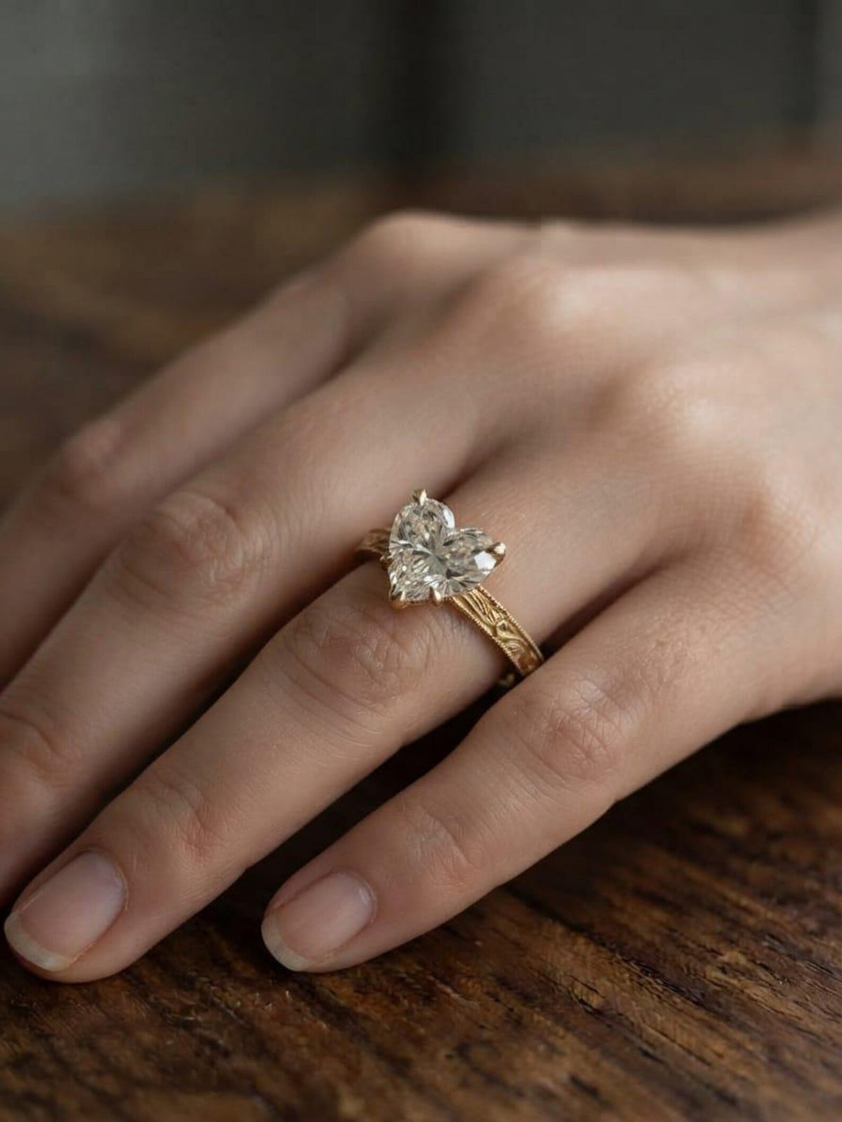 Person wearing a 2 CT heart lab-grown diamond engagement ring featuring an intricate vintage hand-carved yellow gold band.