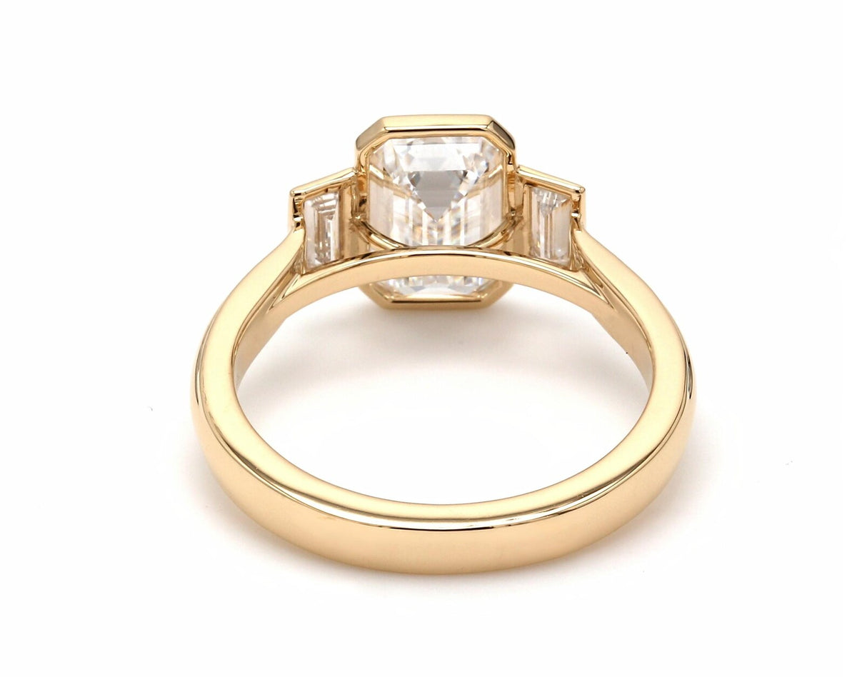 Underneath view of yellow gold bezel frame holding a 4 carat emerald lab-grown diamond and baguette side stones.