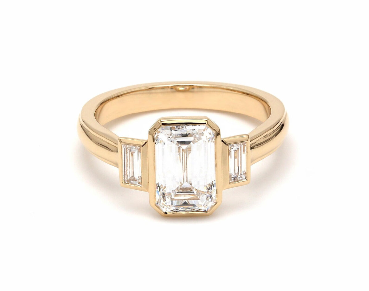Front view of 4 CT emerald cut lab-grown diamond bezel ring with baguette side stones in 14K yellow gold.