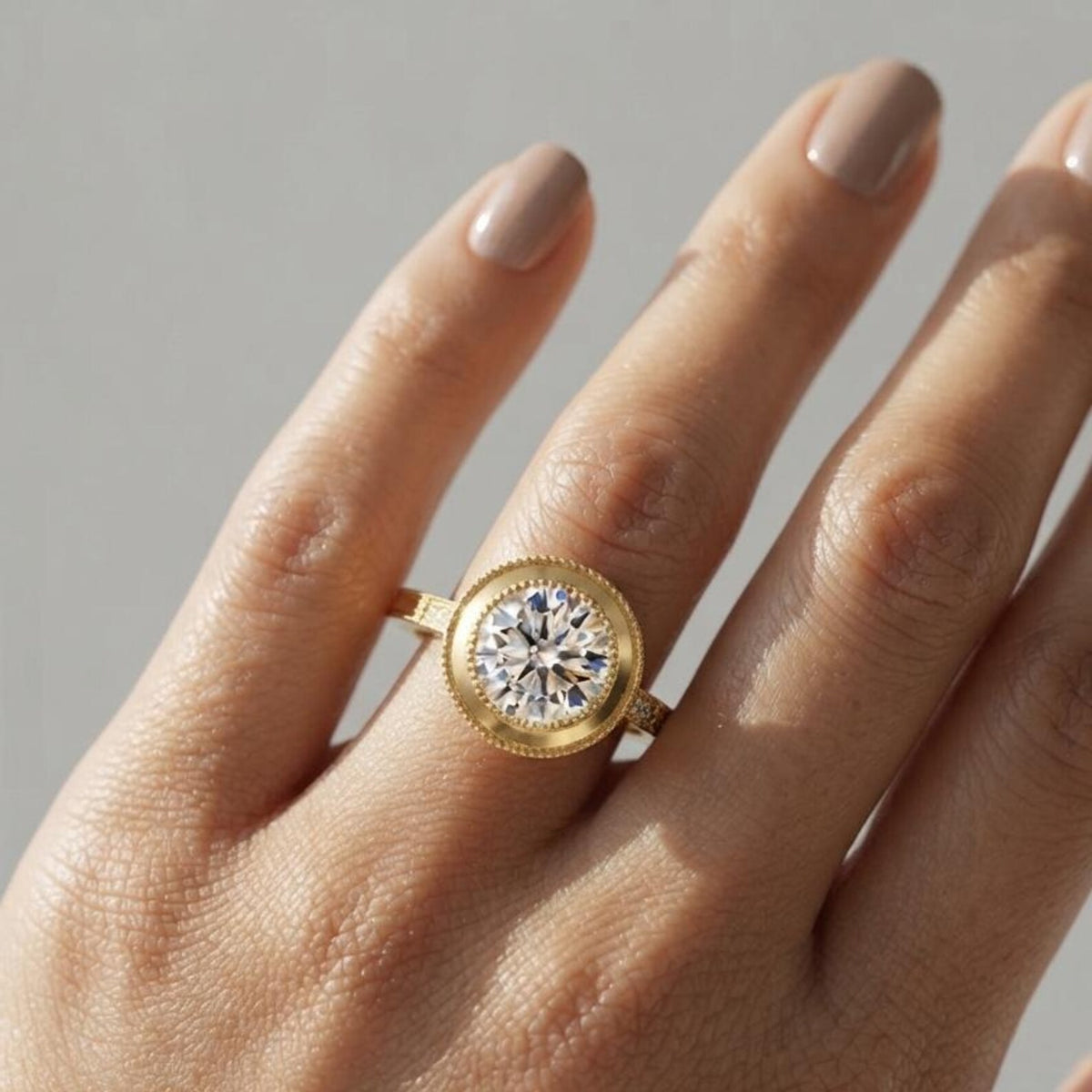On-finger view of a 3 CT round lab grown diamond engagement ring set in a textured yellow gold milgrain bezel.