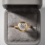 3 carat round brilliant lab grown diamond bezel ring in yellow gold resting inside a plush gray velvet ring box.