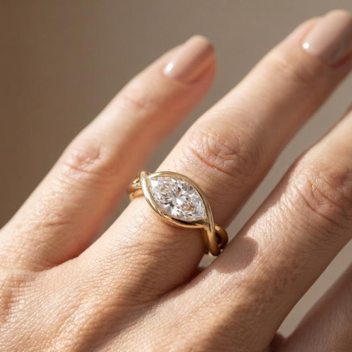 On-finger view of a 2 CT horizontal marquise lab grown diamond engagement ring with a smooth yellow gold swirl bezel.