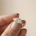 Close-up of a hand holding a 2 CT east-west marquise lab created diamond ring showing the sleek yellow gold bypass band.