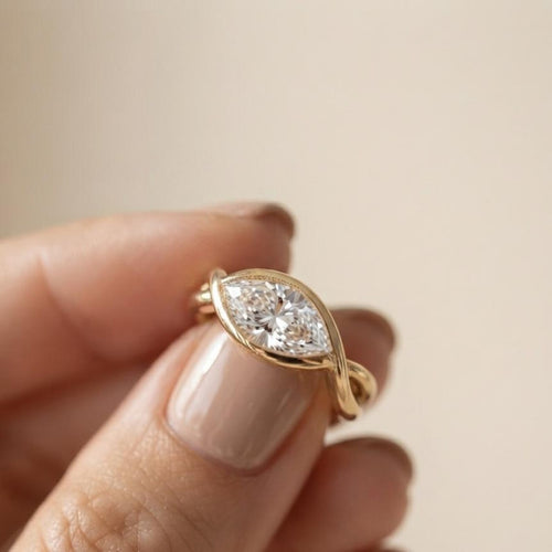 Close-up of a hand holding a 2 CT east-west marquise lab created diamond ring showing the sleek yellow gold bypass band.