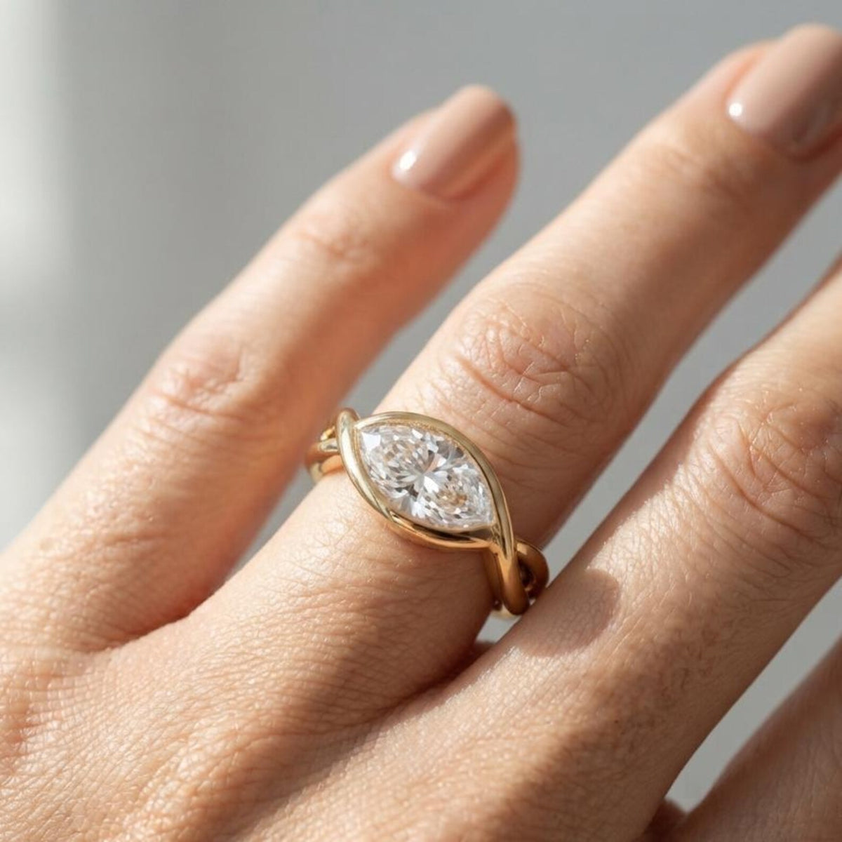 Bright lifestyle view of a 2 carat marquise lab diamond bezel ring in yellow gold worn on a finger under natural light.