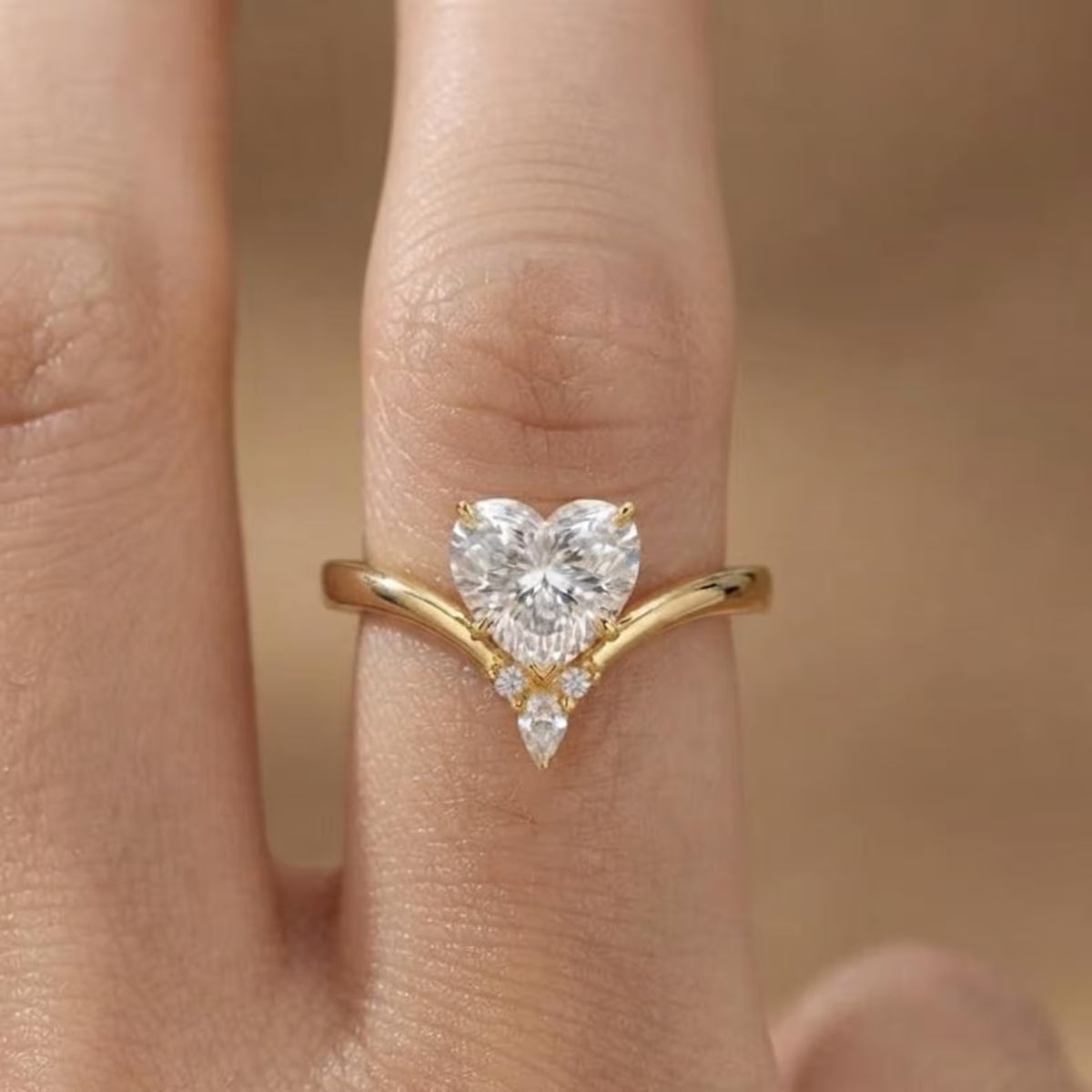 On-finger view of a 2 CT heart cut lab grown diamond engagement ring with a yellow gold chevron band and diamond accent cluster.