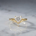 2 carat heart-shaped lab diamond chevron engagement ring in yellow gold set on a reflective white marble surface.