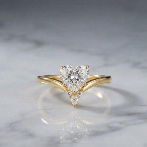 2 carat heart-shaped lab diamond chevron engagement ring in yellow gold set on a reflective white marble surface.