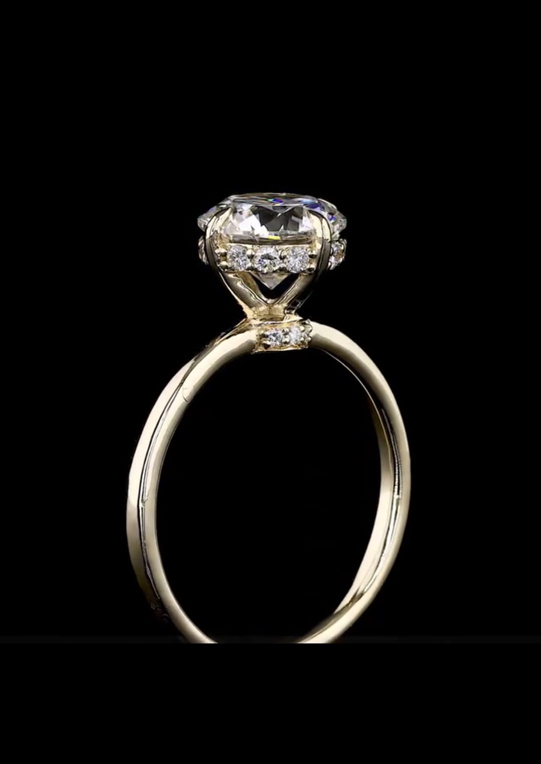Detailed side profile view of a yellow gold round diamond solitaire featuring a diamond hidden halo and pavé accent bridge collar.