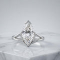 3 CT marquise lab grown diamond engagement ring in platinum with a split shank setting resting on a white marble surface.