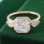 3 CT Asscher lab grown diamond three-stone ring with bezel-set pear side diamonds in yellow gold on green velvet.
