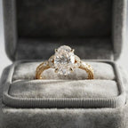 4 CT oval lab grown diamond engagement ring with hand-engraved yellow gold vintage band displayed in a plush gray velvet box.