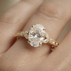 On-finger view of a 4 carat oval lab diamond ring with marquise leaf-cluster side accents and filigree milgrain band in yellow gold.