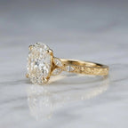 Side profile view of a 4 CT oval lab grown diamond ring on white marble showing intricate vintage scroll engraving on yellow gold.